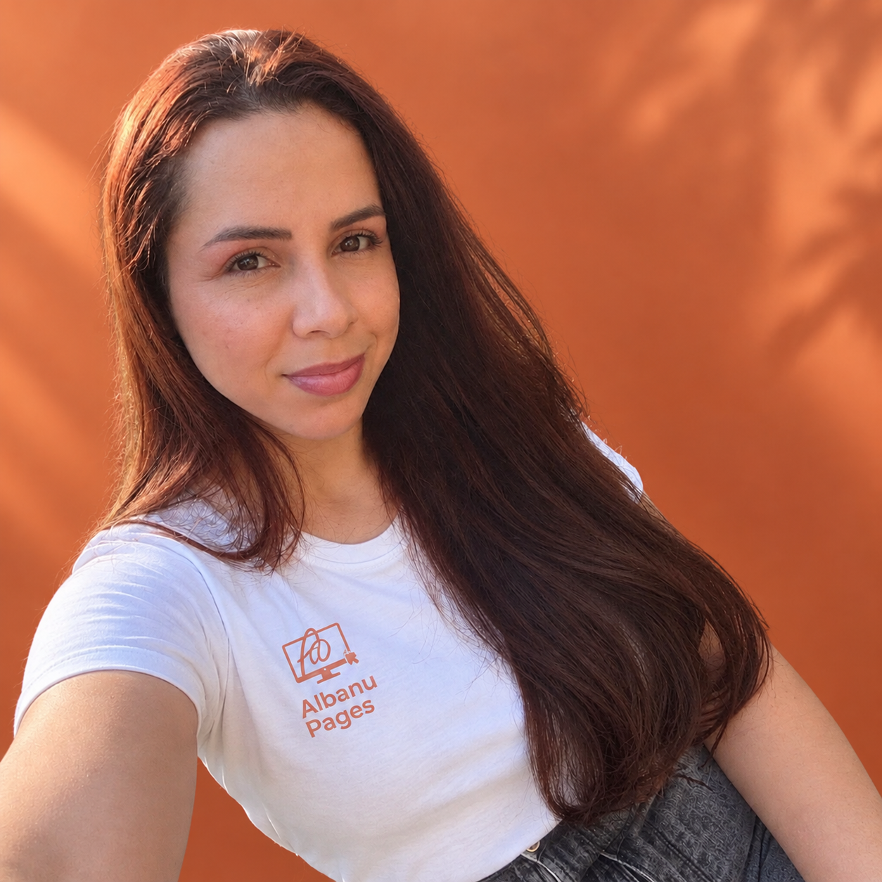 Caroline Albano Domingues, fundadora da Albanu Pages, com camiseta branca da marca sobre fundo terracota